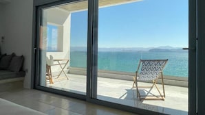Ein modernes Zimmer mit einer Schiebeglastür, die auf einen Balkon mit Blick auf das Meer und die Berge führt.