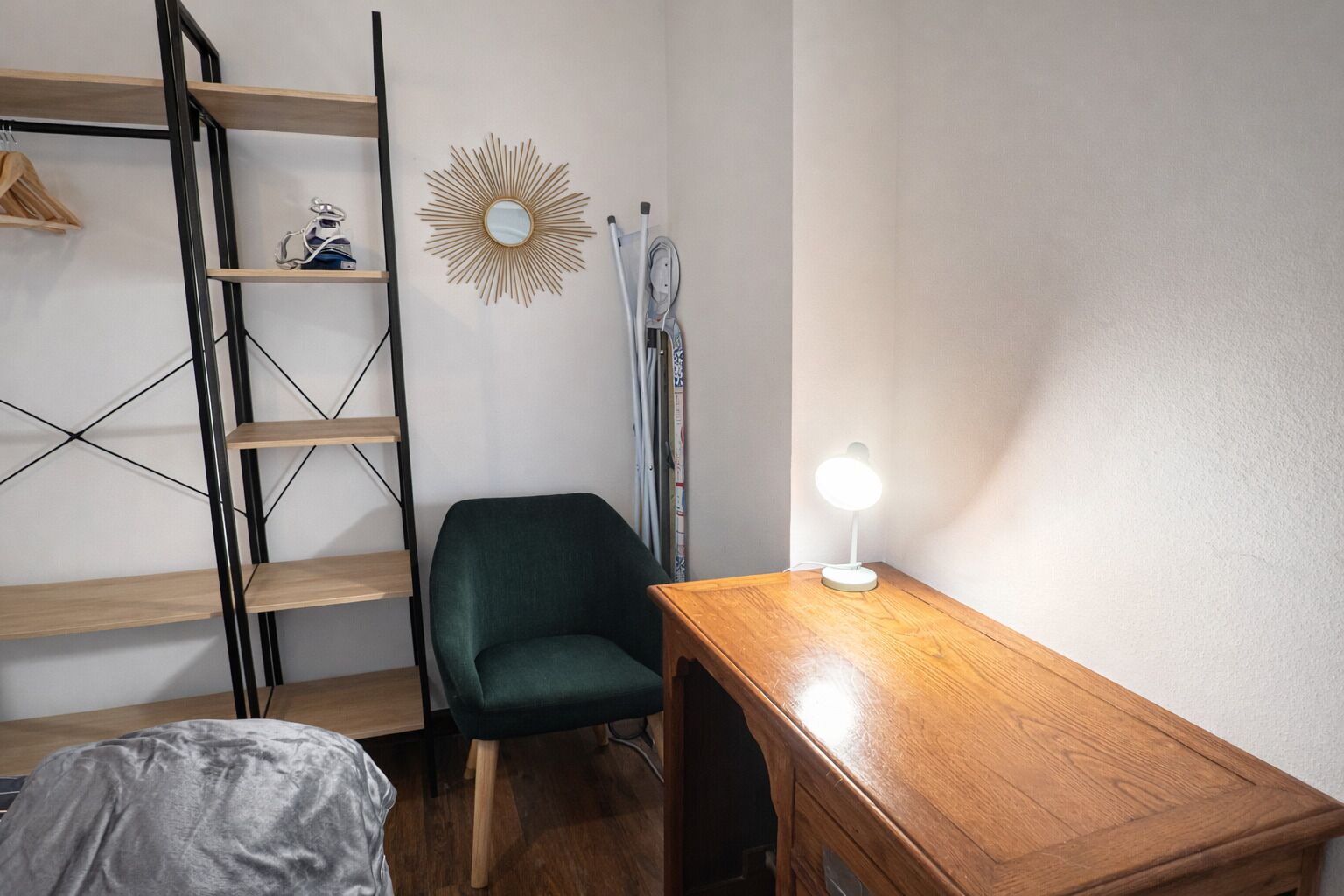 Une petite pièce comprenant un bureau en bois, une chaise verte, une étagère en bois et un miroir fixé au mur.