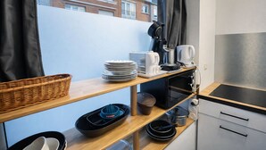 A compact kitchen with a microwave, kettle, and coffee maker on a wooden shelf, a basket, and stacked plates. - Parenthèse Urbaine in Armentières (Armentières)
