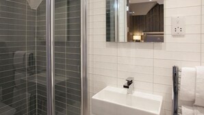 Ein modernes Badezimmer mit Duschkabine aus Glas, einem weißen Waschbecken und einem Spiegel, der ein Holzinnere widerspiegelt.