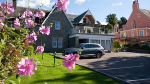 Ein Steinhaus mit einem modernen Anbau, einem parkenden Auto und einem Garten mit rosa Blumen.