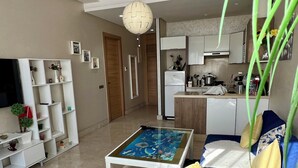 A modern living room with a blue sofa, a coffee table with a blue and white pattern, and a small round rug. There is a kitchen area in the background with a white refrigerator and a sink.