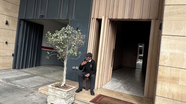 A man sitting on a stool outside a building with a potted plant nearby.