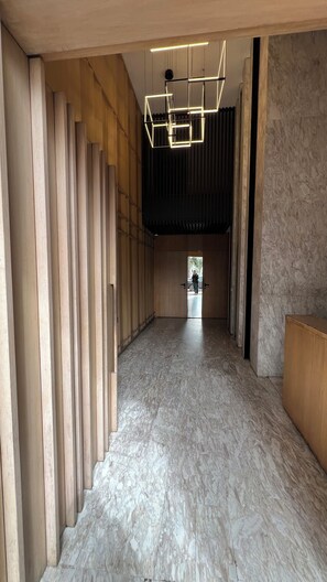 Un pasillo con listones de madera en un lado, suelo de mármol y una lámpara con diseño geométrico.