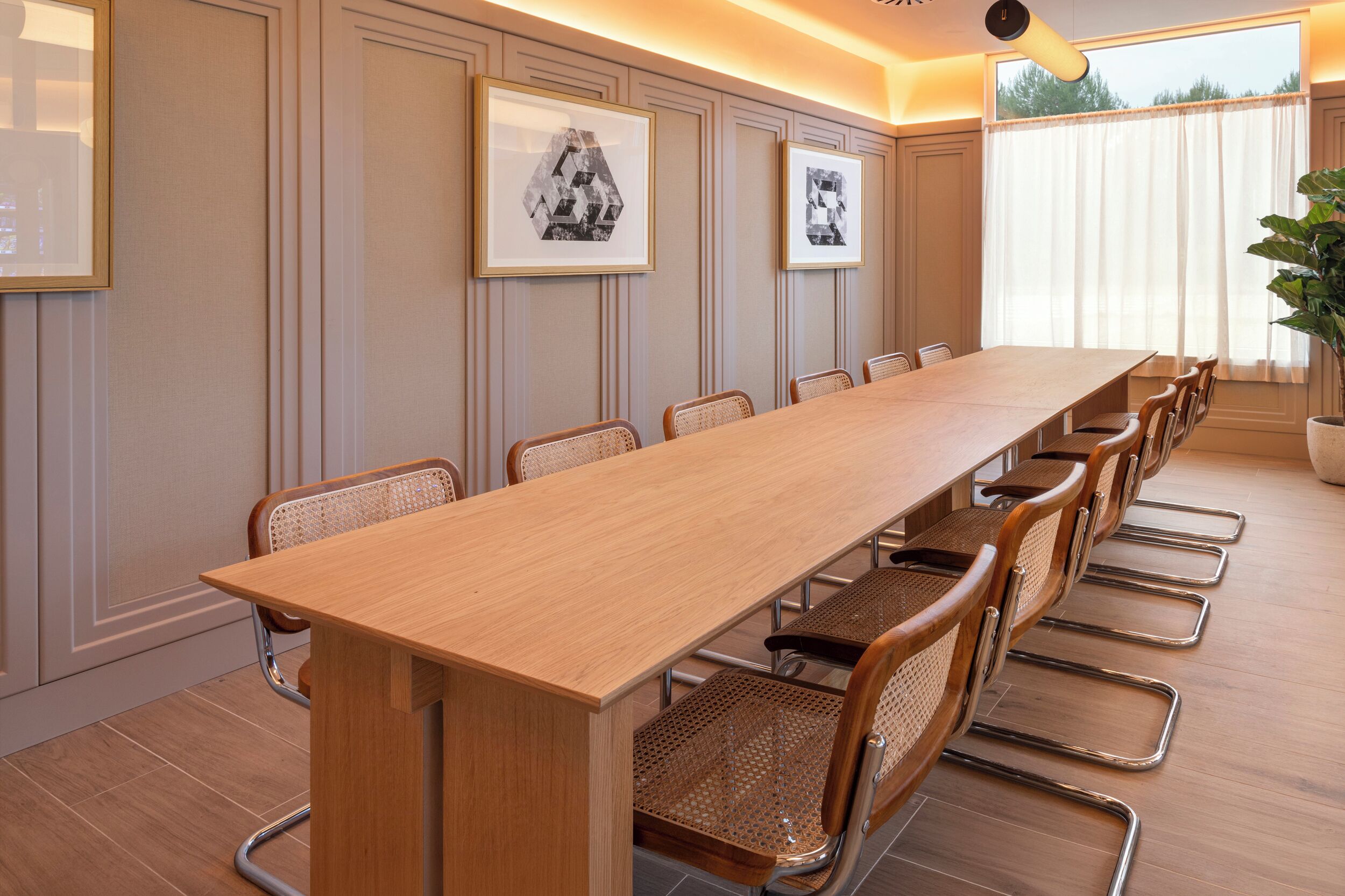 A conference room with a long wooden table, wicker chairs, and framed pictures on the wall.