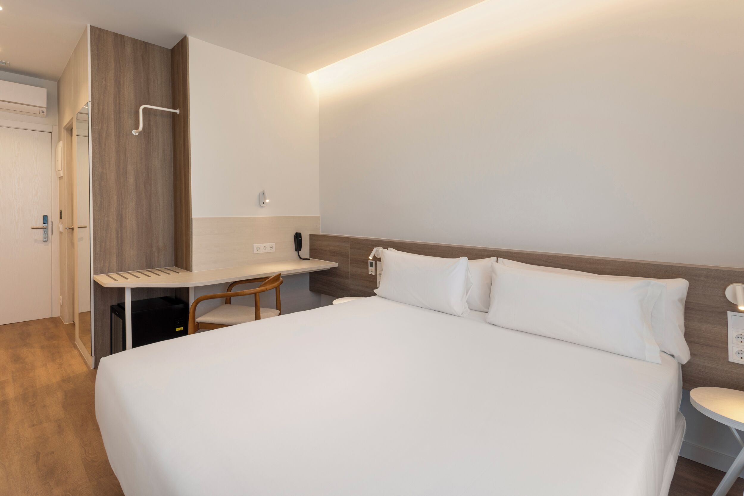 A modern hotel room with a large bed, a desk, and a chair.