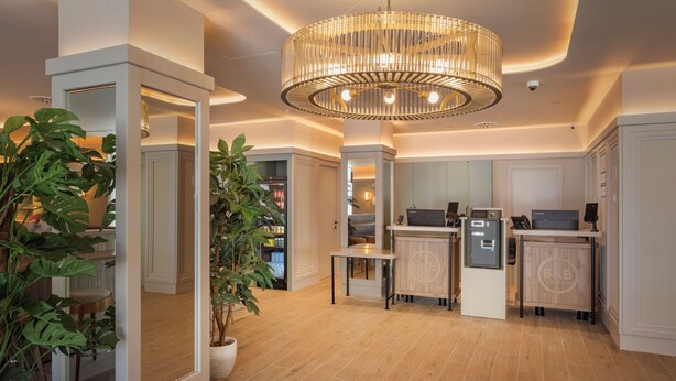 A modern kitchen with wooden flooring, a central island, built-in appliances, and a large chandelier. - B&B HOTEL Madrid Vallecas Ensanche (Madrid)