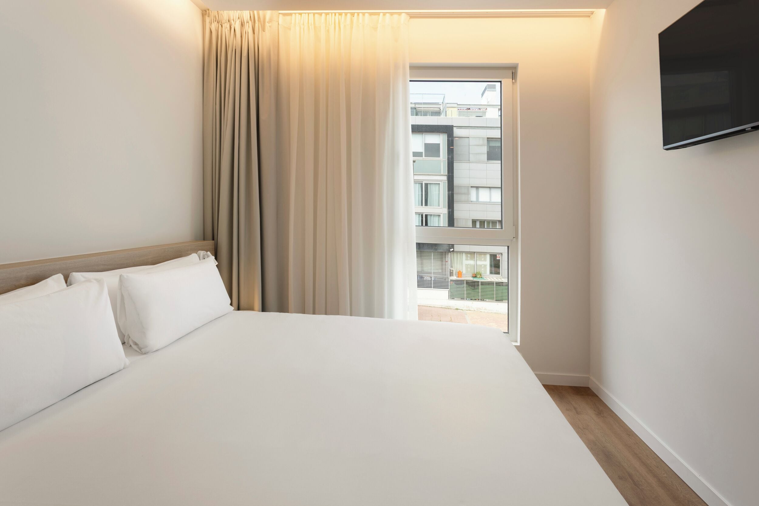 Une chambre d’hôtel avec un grand lit, une fenêtre avec des rideaux et un téléviseur à écran plat fixé au mur.