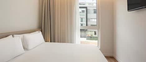 A hotel room with a large bed, a window with curtains, and a flat-screen TV mounted on the wall.