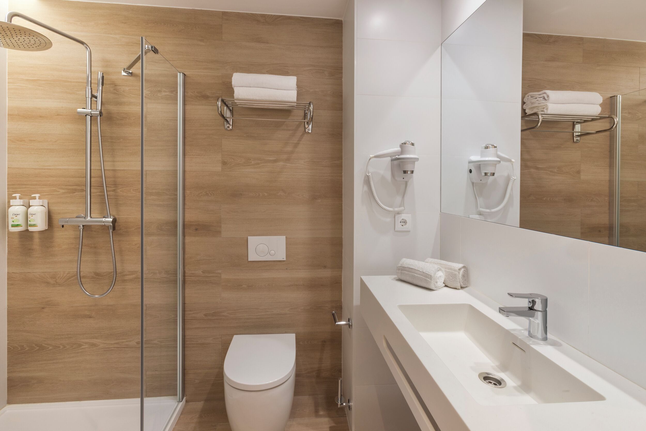 Un baño moderno con ducha envuelta en vidrio, inodoro blanco y tocador con lavamanos y espejo.