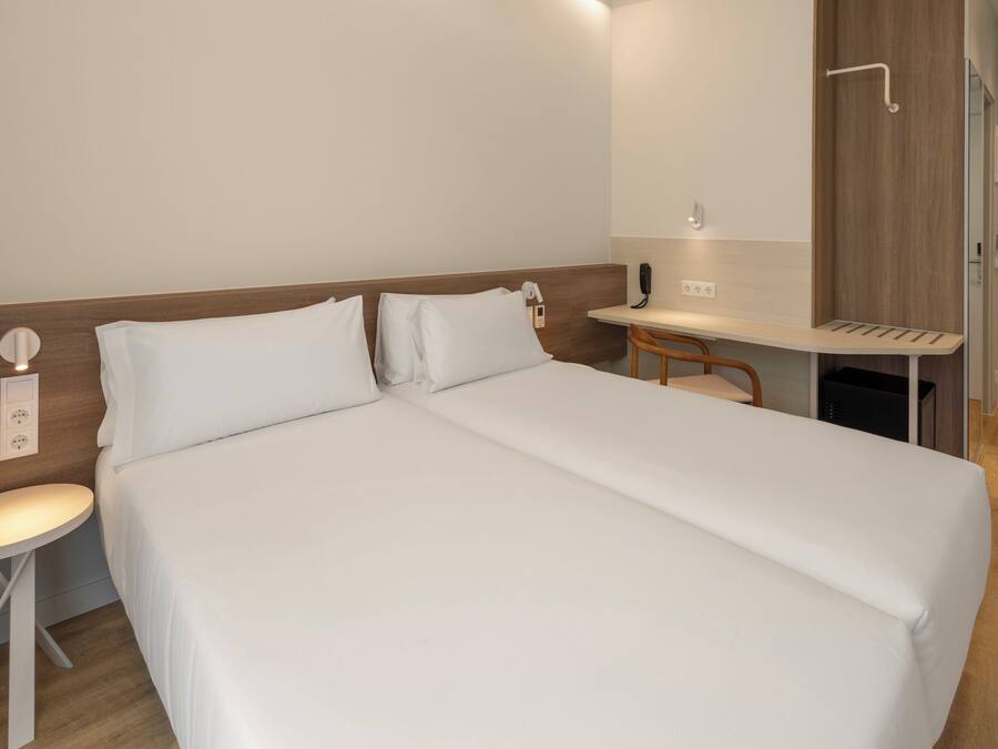 A hotel room with a bed, a desk, a chair, and a small table.