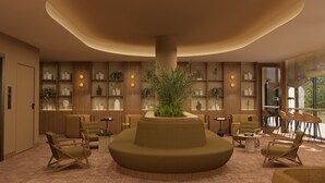 Ein moderner Lounge-Bereich mit einer zentralen, runden Sitzgruppe, umgeben von Bücherregalen und einer großen Pflanze in einem Topf.