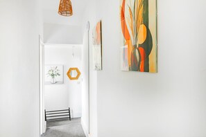 A hallway with a white wall, a hexagonal mirror, a framed picture, and abstract art. - Modern Gem in the heart of Nottingham City Centre (Nottingham)