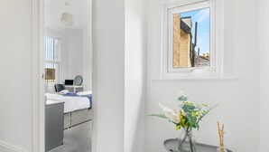 Hotellihuone, jossa on sänky, työpöytä kannettavalla tietokoneella, ikkuna, josta on näkymä rakennuksiin, ja pienellä pöydällä oleva maljakko, jossa on kukkia.