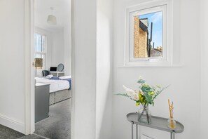 A hotel room with a bed, a desk with a laptop, a window with a view of buildings, and a vase with flowers on a small table. - Modern Gem in the heart of Nottingham City Centre (Nottingham)