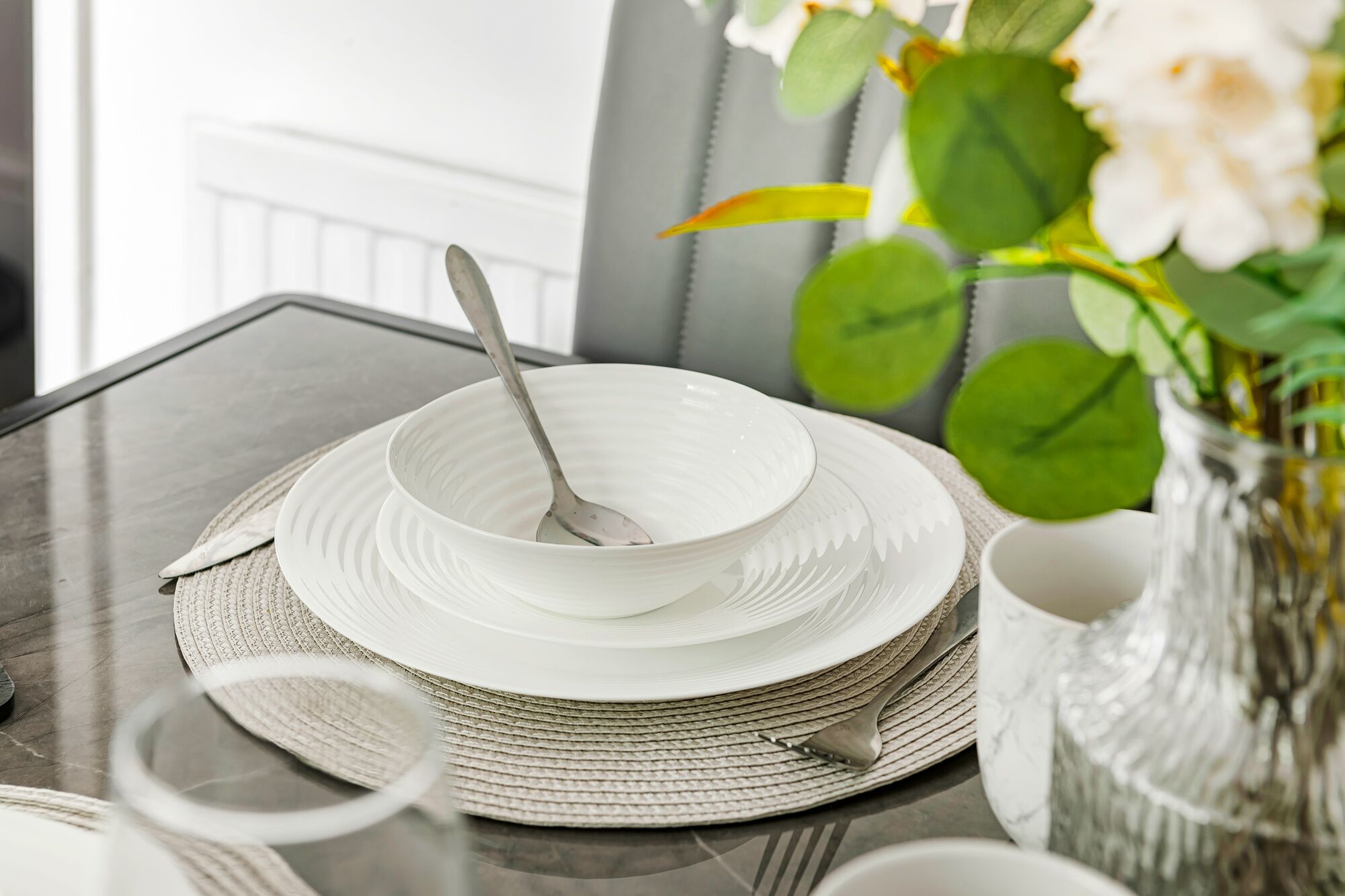 Una mesa de comedor con platos blancos, un tazón y una cuchara.