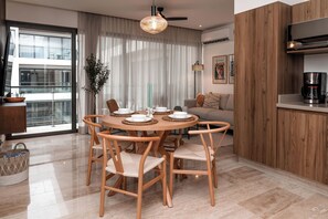 A modern dining area with a round wooden table, six chairs, and a hanging light fixture. - Playa's Golden Area- 2BR2BA modern tropical retreat, beach, Infinite Pool, Gym (Playa del Carmen)