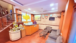 A reception area with a reception desk, seating, a staircase, and a wall-mounted television. - ShivSagar Residency Zaveri Bazaar (Mumbai)