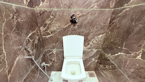 A bathroom with a marble wall, a toilet, and a shower. - ShivSagar Residency Zaveri Bazaar (Mumbai)
