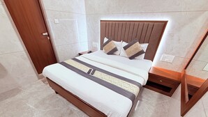 A neatly made bed with a headboard, a bedside table, and a power outlet on the wall. - ShivSagar Residency Zaveri Bazaar (Mumbai)