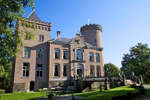 Un grande edificio storico con una torre imponente, numerose finestre e un prato curato.