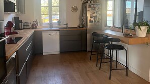 Een moderne keuken met een vaatwasser, een spoelbak en een koelkast. Er staan twee barkrukken en een raam met uitzicht op het buitengebied.