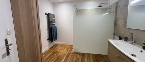 A modern bathroom with a wooden floor, a white sink, a mirror, and a shower.