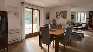 Een ruime woonkamer met een houten eettafel, comfortabele zithoek, een groot raam en een gezellige open haard.