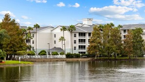 A hotel with a water fountain, a lake, and a well-maintained lawn with palm trees. - 2 BR Deluxe Condo at Wyndham Cypress Palms (Kissimmee)