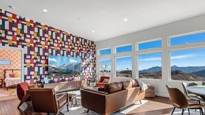 Una sala de estar moderna con una pared de diseño geométrico y colorido, un ventanal con vistas a la montaña y una zona de estar acogedora.