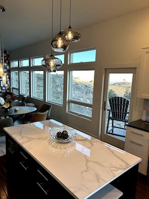 Una cocina moderna con encimera de mármol, luces colgantes y ventanas amplias que ofrecen vistas al exterior.