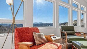 Una sala de estar moderna con ventanas amplias, un sofá rojo, un sillón verde y una mesa de centro de madera.