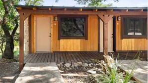 Une cabane en bois avec une seule porte, deux fenêtres et une terrasse en bois.