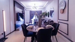 A modern dining area with a round table, black chairs, and a chandelier. - Valyron Homes (Accra)