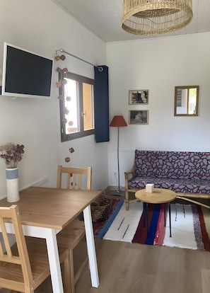 A modern living room with a wooden dining table, chairs, a patterned sofa, a small round table, and a floor lamp. - Studio "Little Nest for Travelers" with Private Terrace, Wi-Fi, and Air Conditioning (Cayriech)