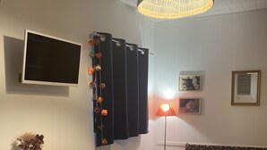 Olohuone, jossa on puinen pöytä, tuoleja, sohva, televisio, lamppu ja riippuvalaisin.