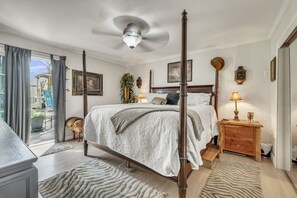 Un dormitorio con cama con dosel, ventilador de techo, mesita de noche con lámpara y vistas al exterior.