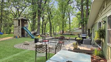 Un jardin avec un espace de jeux, un coin salon extérieur et un barbecue.