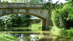 Un puente de piedra sobre un río tranquilo, con abundante vegetación a ambos lados.