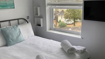 Une chambre à coucher avec un lit, une fenêtre avec des stores, un téléviseur à écran plat et un tableau accroché au mur.