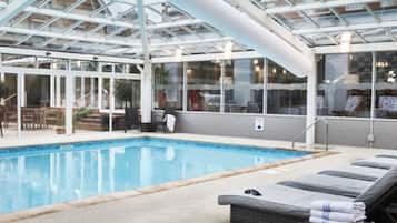 Une piscine dotée de chaises longues et surmontée d’un toit en verre.