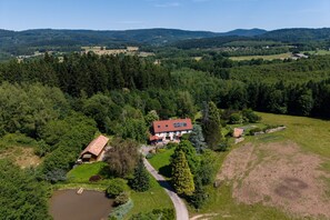 An aerial view of a rural property with a main house, a pond, and surrounding forested areas.