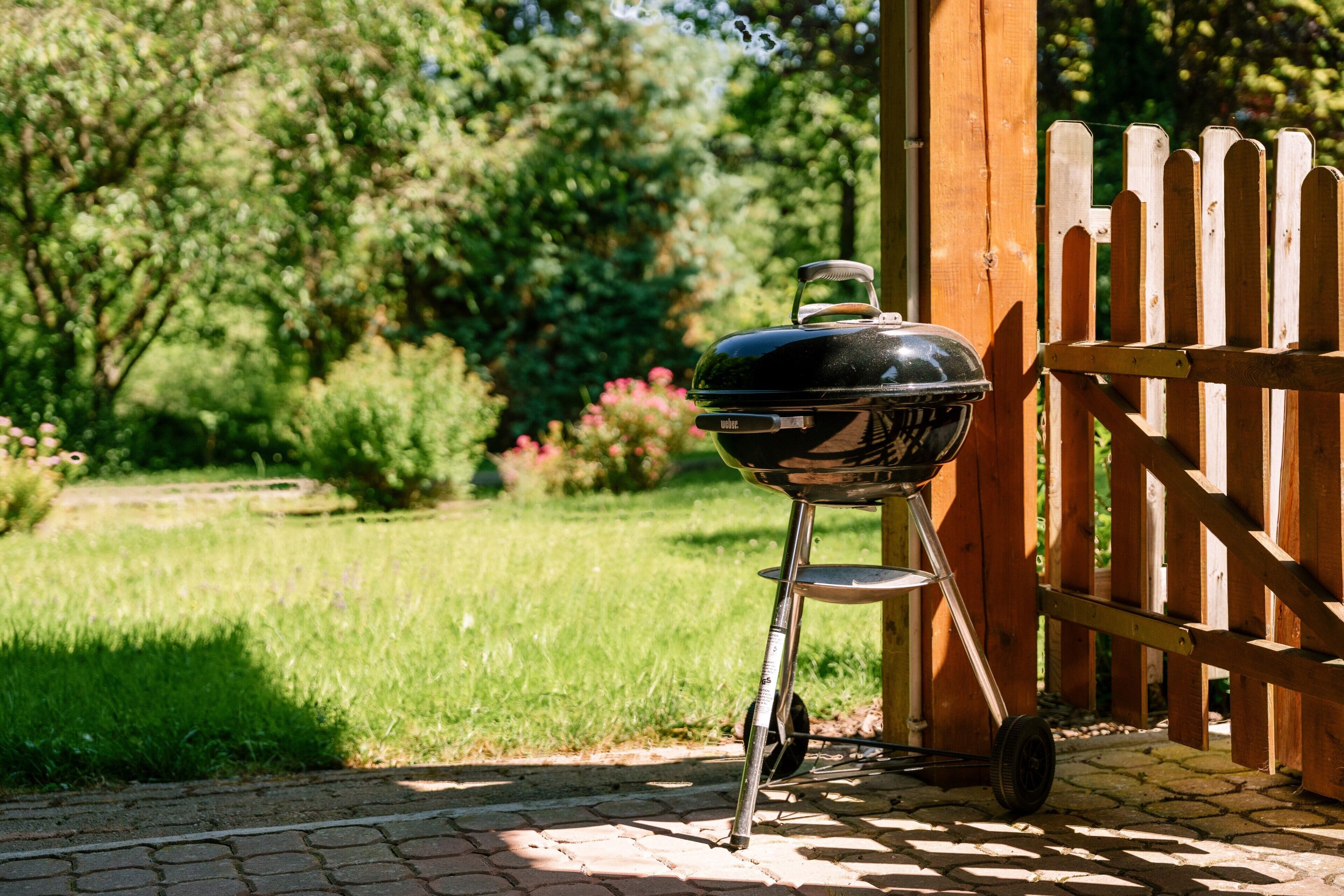 A barbecue grill outdoors with a wooden fence and greenery in the background.