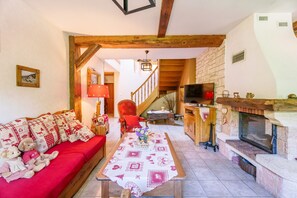 Un salon chaleureux avec un canapé rouge, un escalier en bois, une cheminée et un téléviseur.