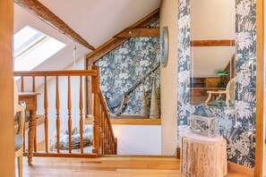 Un escalier en bois avec un puits de lumière, un panier en osier posé sur la plateforme, et un petit tabouret en bois.