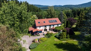 Een huis met een rood dak, omringd door een verzorgde tuin en een dicht bos.
