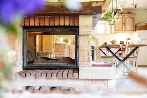 A stone fireplace with a brick base, a wooden mantel, and a glass door. - Gîte "Gîte de La Pieviche" with Mountain View, Wi-Fi, and Air Conditioning (on request) (Provenchères-et-Colroy)