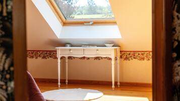 Een kamer met dakraam, een wit bureau met lades, een bloemenrand op de muur en een witte vloerkleed.