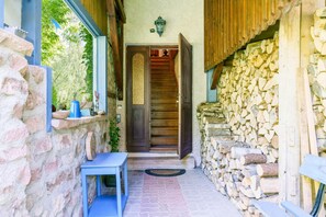 Un mur de pierre, une porte en bois, un banc et une pile de bûches.