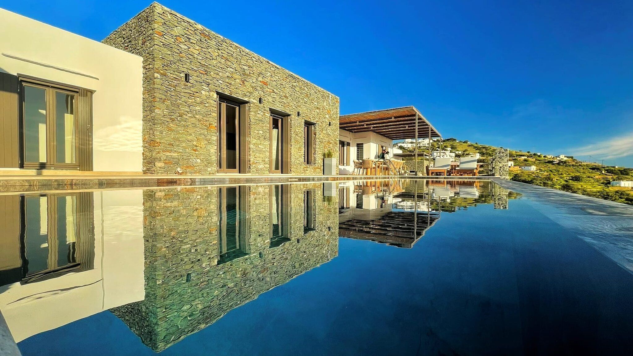 Eine moderne Villa mit Natursteinfassade, einem Swimmingpool und einem klaren Spiegelbild.